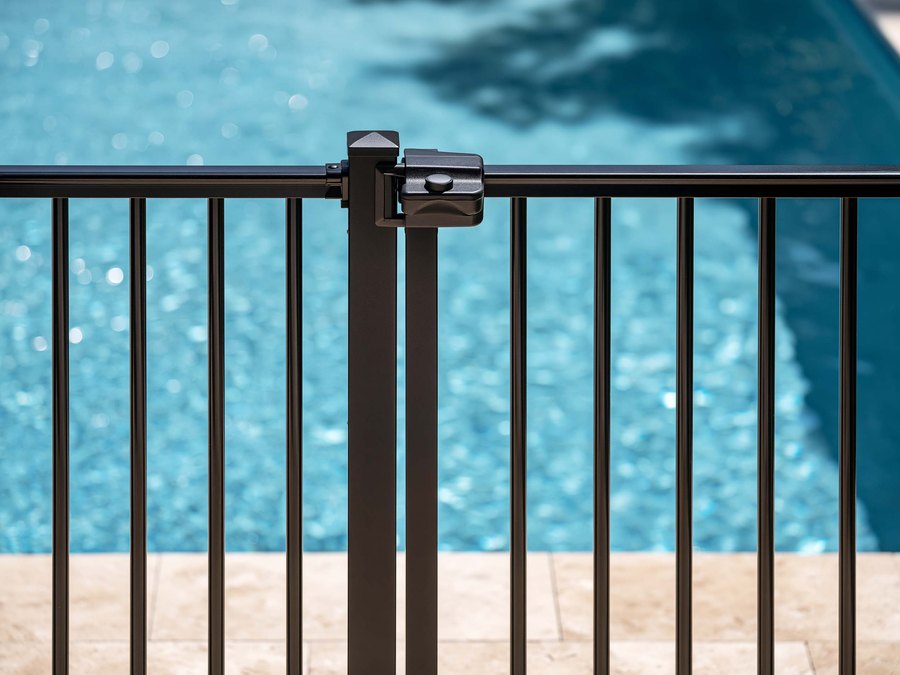 A push-button pool gate latch at the top of the gate, with the deck in view below it